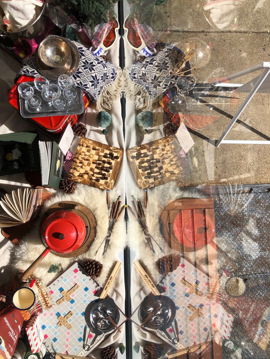 an image of a window display with various items on it such as a red pot, a wooden chess game, scrabble, and books.