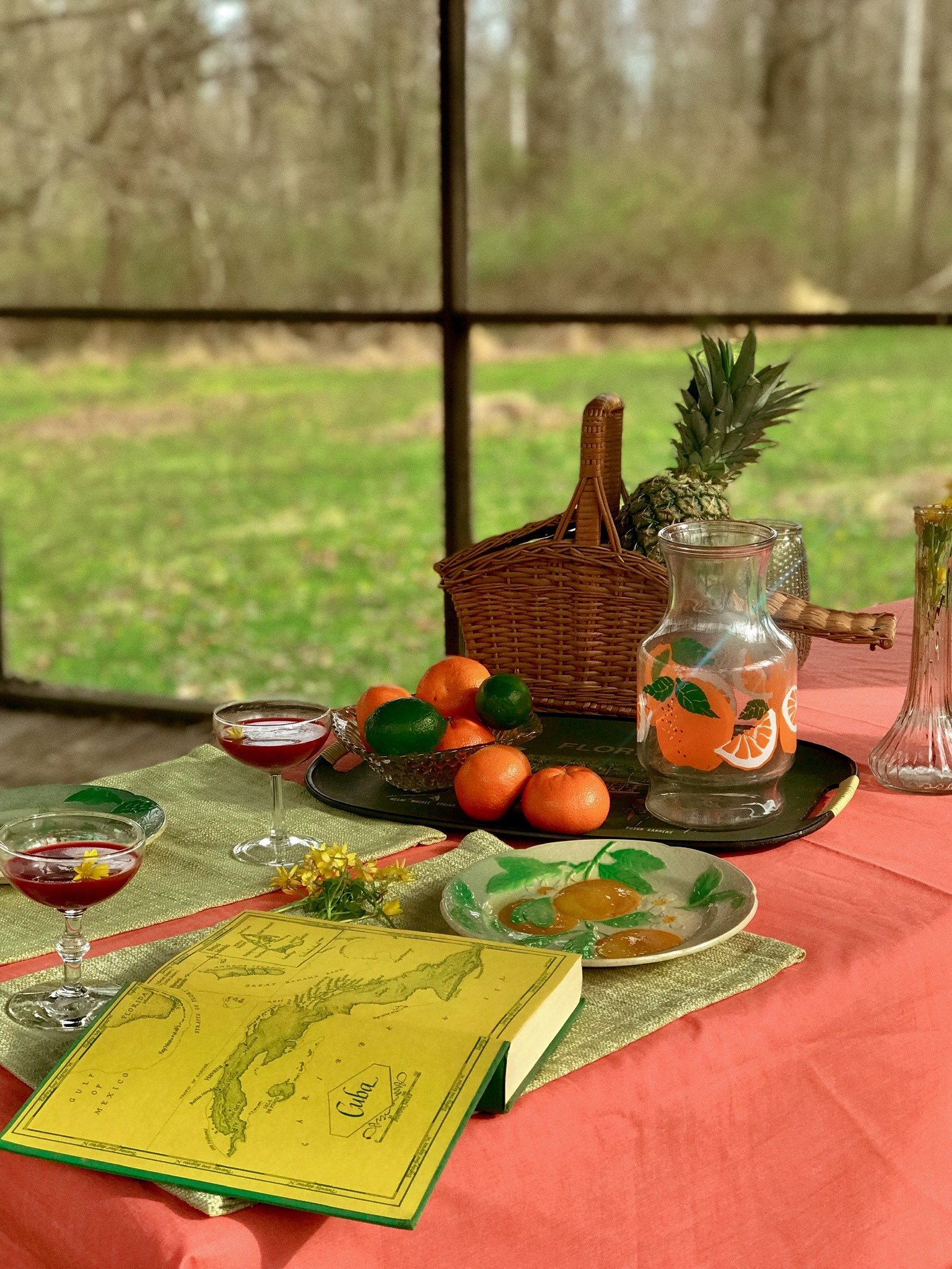 a table set up with a book, a basket of fruit, and a glass of wine