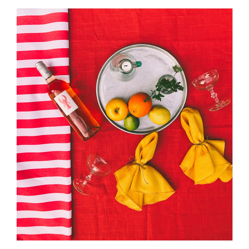 red and yellow napkins, wine glasses and oranges on a red and white striped tablecloth